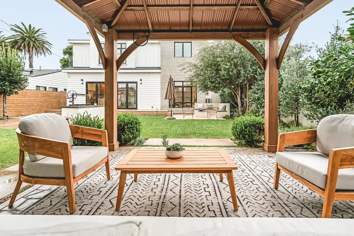 Completed backyard viewed from a shaded timber pergola, with lounge chairs and a planted lawn